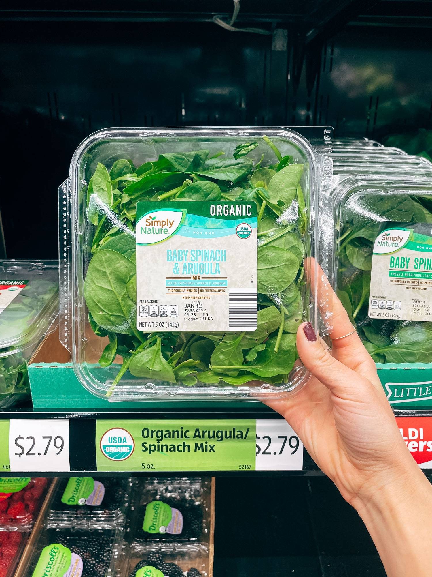 White hand holding package of spinach and arugula