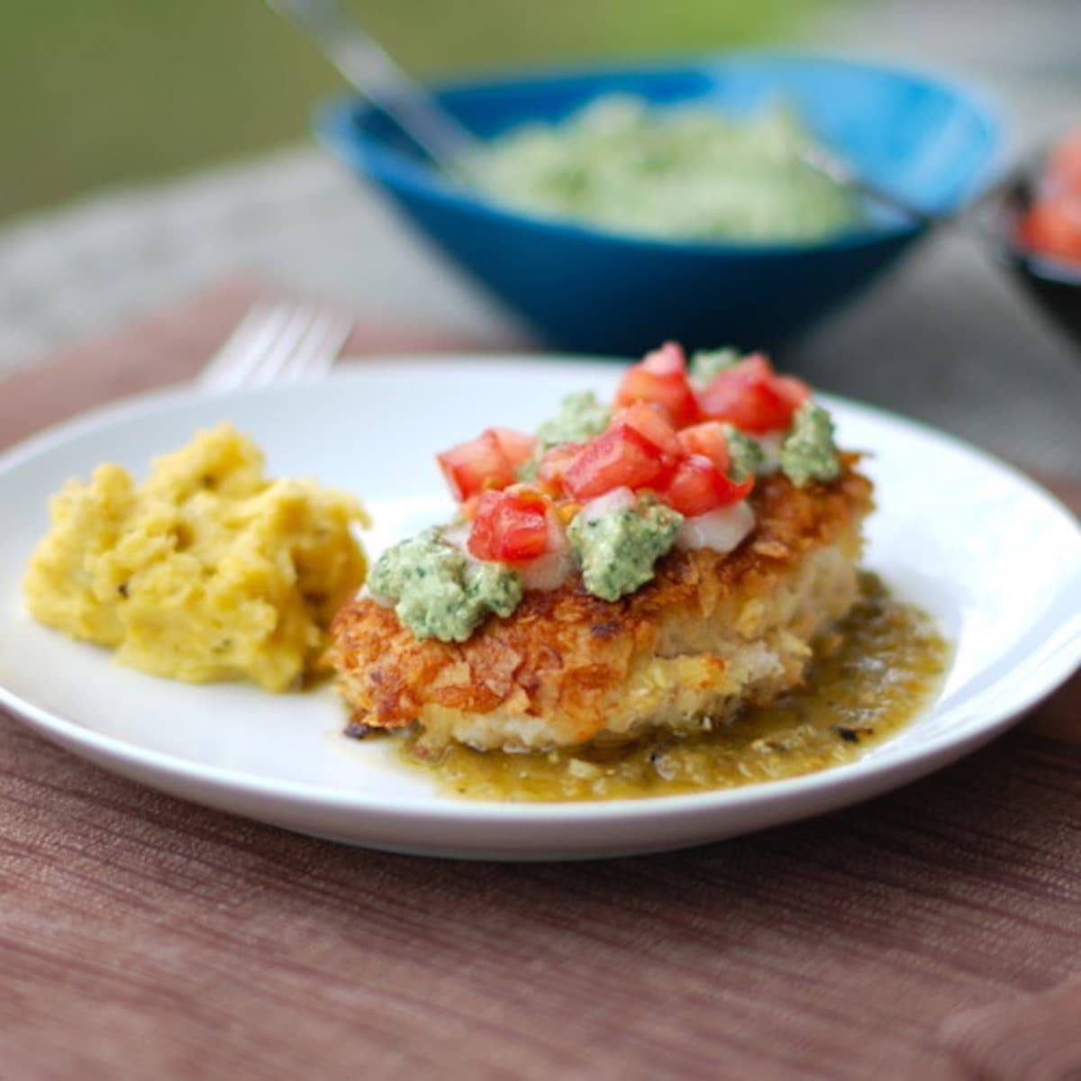 Tortilla chicken with salsa verde is chicken coated with corn tortilla chips and topped with salsa verde on a white plate.