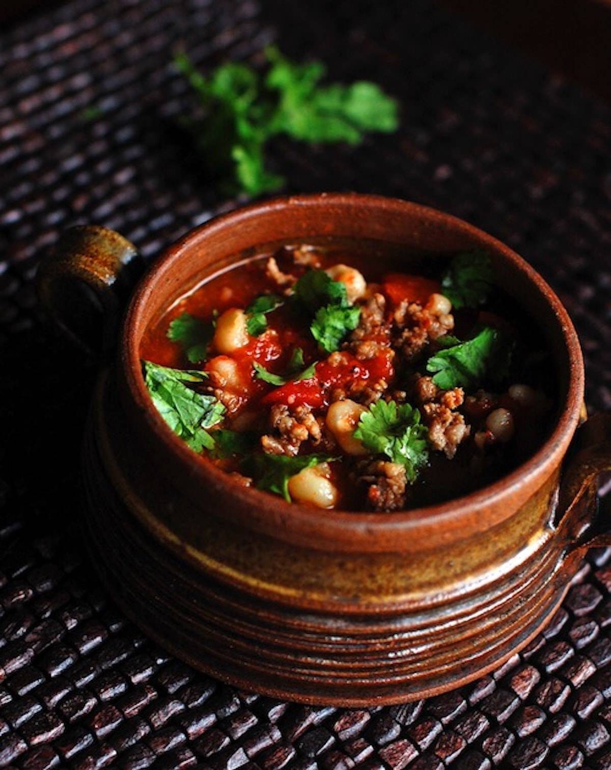 Spicy sausage posole in a unique bowl with herb topping.